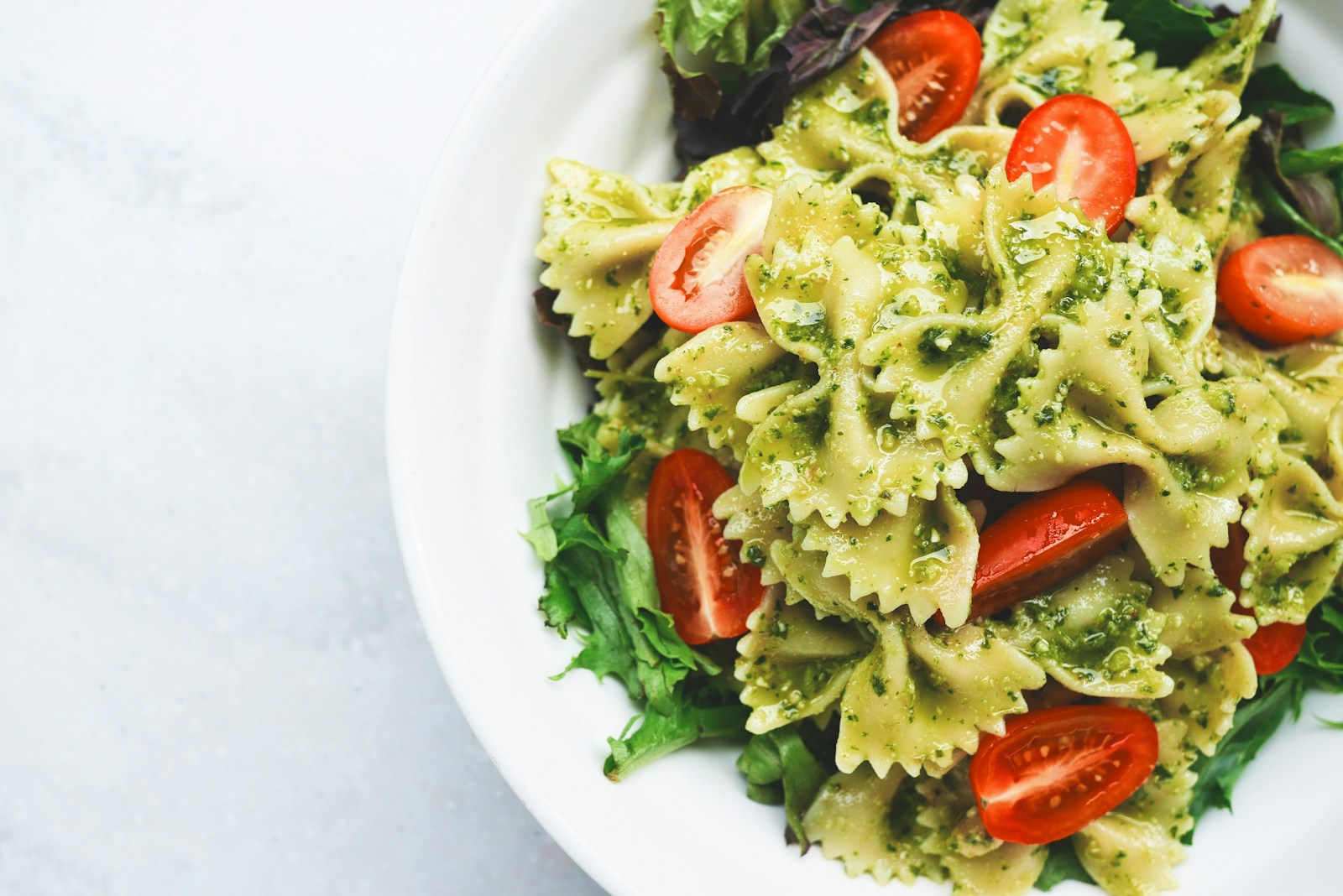 Farfalle in a green herb sauce on a white plate, with tomato and salad leaves.